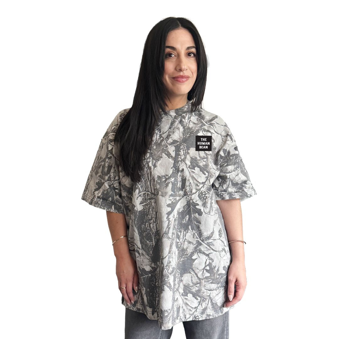 Woman wearing a camouflage-patterned shirt with a The Human Bean brand logo on a white background