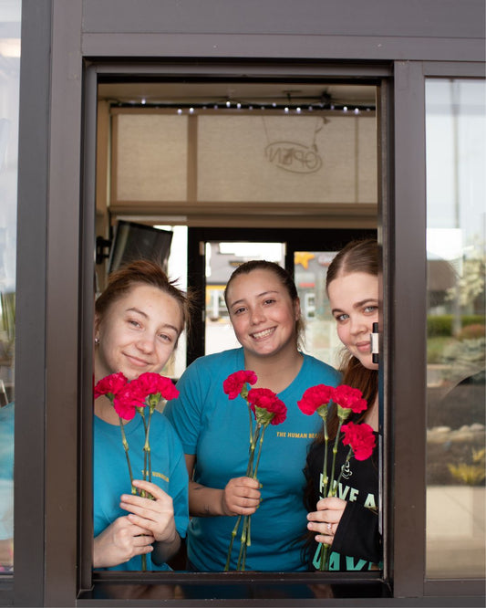 Photo Showing Baristas from The Human Bean Holding Flowers in Celebration of Mother's Day - All moms receive a free flower on Mother's Day at any The Human Bean location while supplies last! 