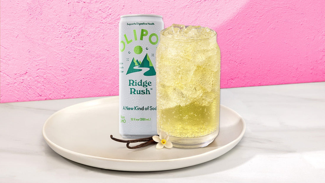 Light yellow drink in a glass with next to a OLIPOP Ridge Rush can on a white plate against a pink background