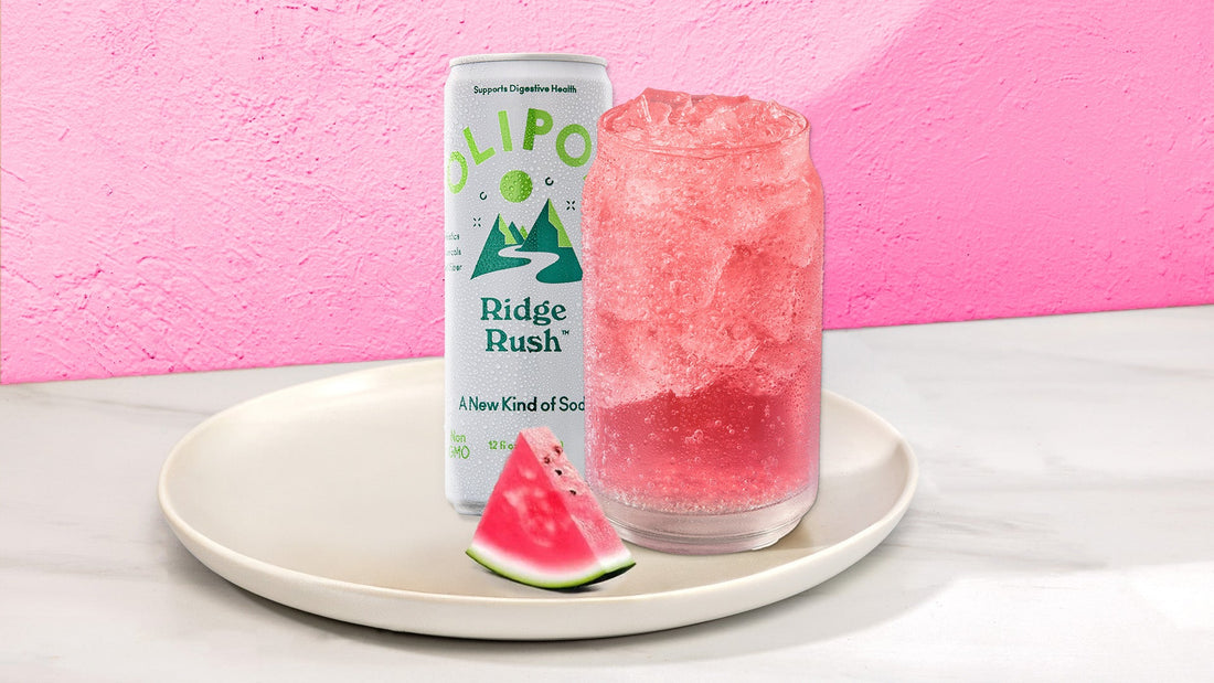 Pink drink in a glass with next to a OLIPOP Ridge Rush can on a white plate with fruit against a pink background