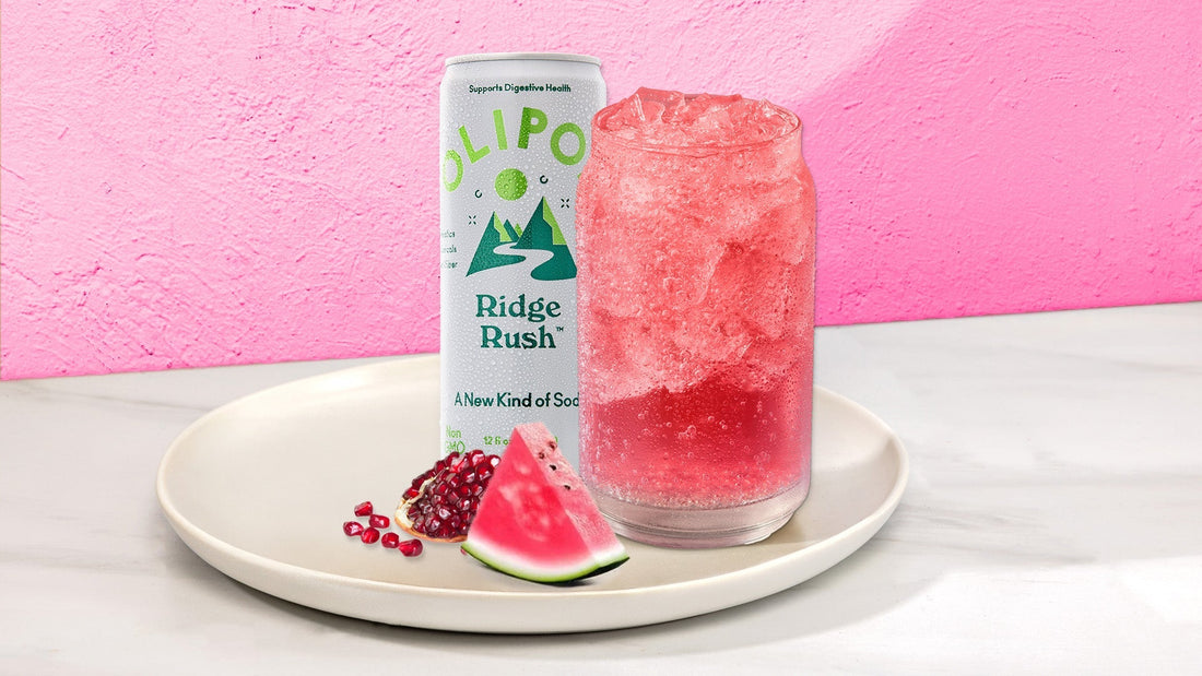 Pink drink in a glass with next to a OLIPOP Ridge Rush can on a white plate with fruit against a pink background