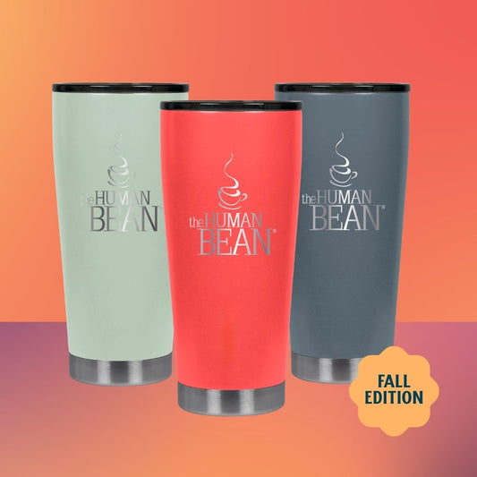 Three insulated travel tumbler cups with lids are shown against a warm orange-to-pink gradient background. The center cup is coral red, the left cup is pale mint green, and the right cup is dark gray.